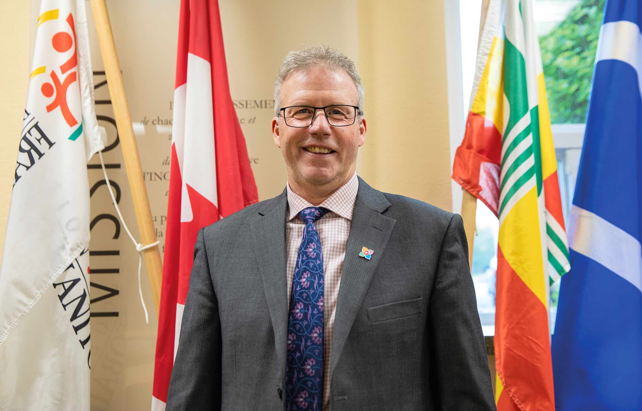 René Déquier devant le drapeau canadien, franco-manitobain et métis.