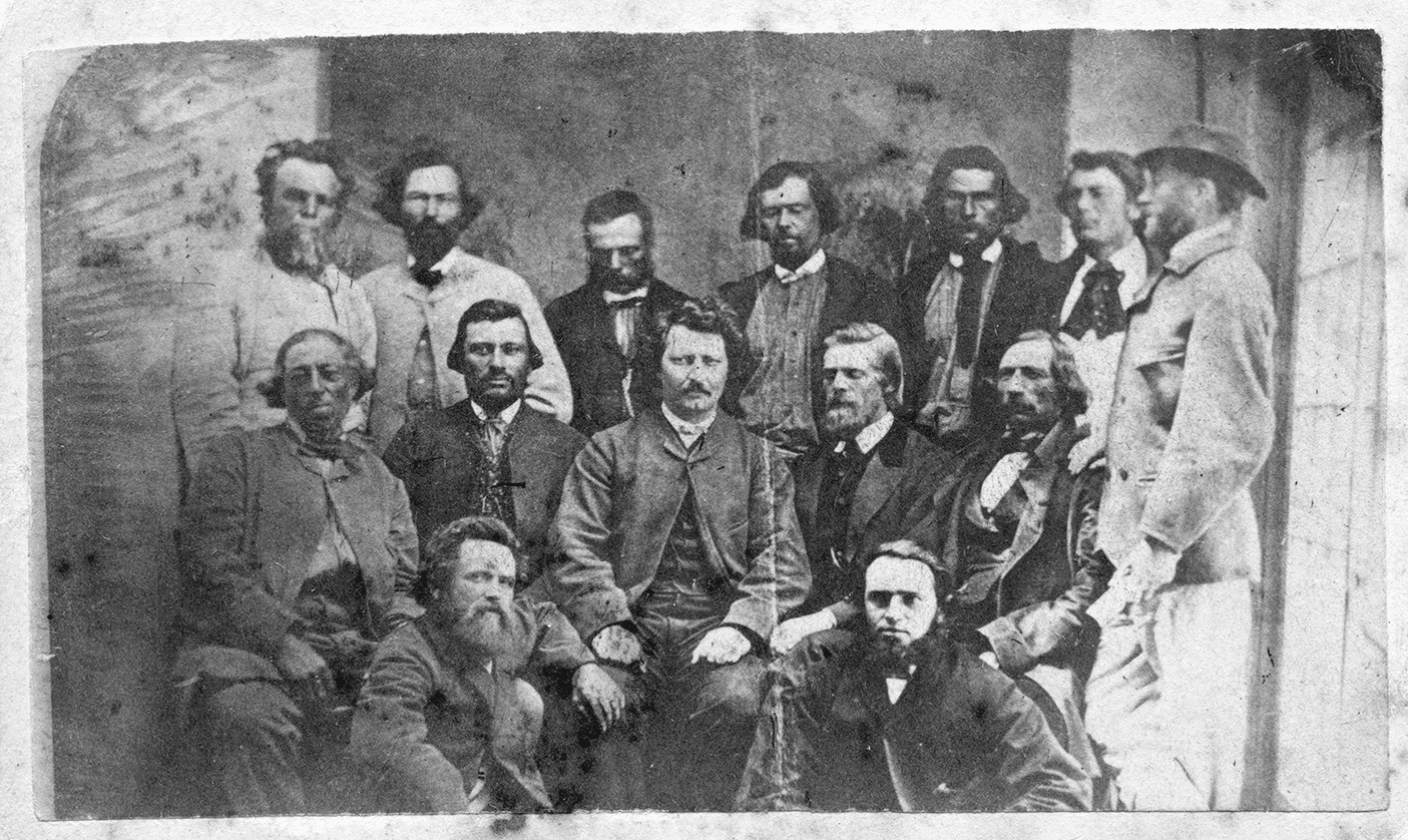 Photographie prise le 3 juin 1870 par Joseph Langevin. À l’arrière-plan, de gauche à droite : François Guillemette (Charles Larocque), Pierre Delorme, Thomas Bunn, Xavier Pagé, André Beauchemin, Baptiste Tourond et Thomas Spence (de profil). Au rang central : Pierre Poitras, John Bruce, Louis Riel, William O’Donoghue et François Dauphinais. Au premier plan : Hugh F. (ou Bob) O’Lone et Paul Proulx. 