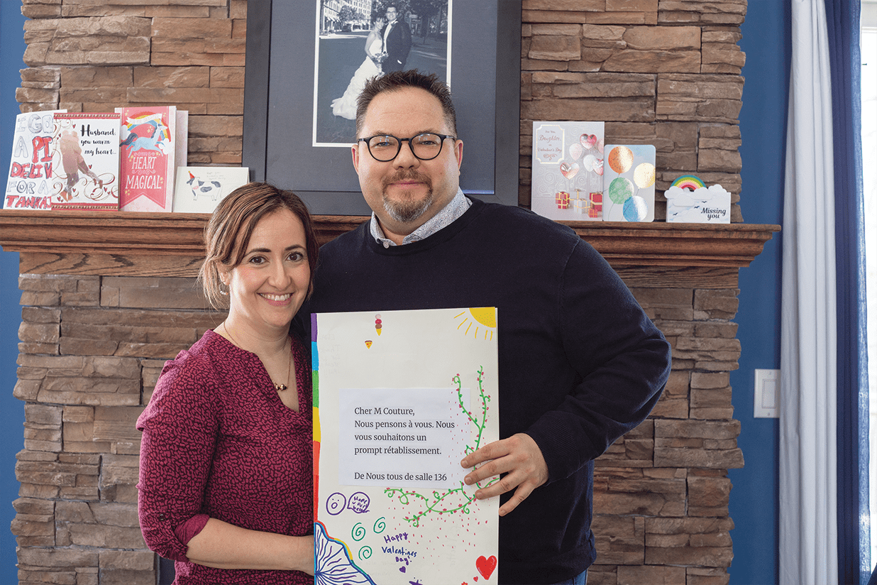 Matt Couture, accompagné de sa conjointe Christina, tient une carte réalisée par ses élèves de la salle 136, lui souhaitant un prompt rétablissement, un geste de soutien qui témoigne de l’impact de sa maladie sur sa vie professionnelle et personnelle, alors que son épilepsie est récemment redevenue difficile à contrôler.