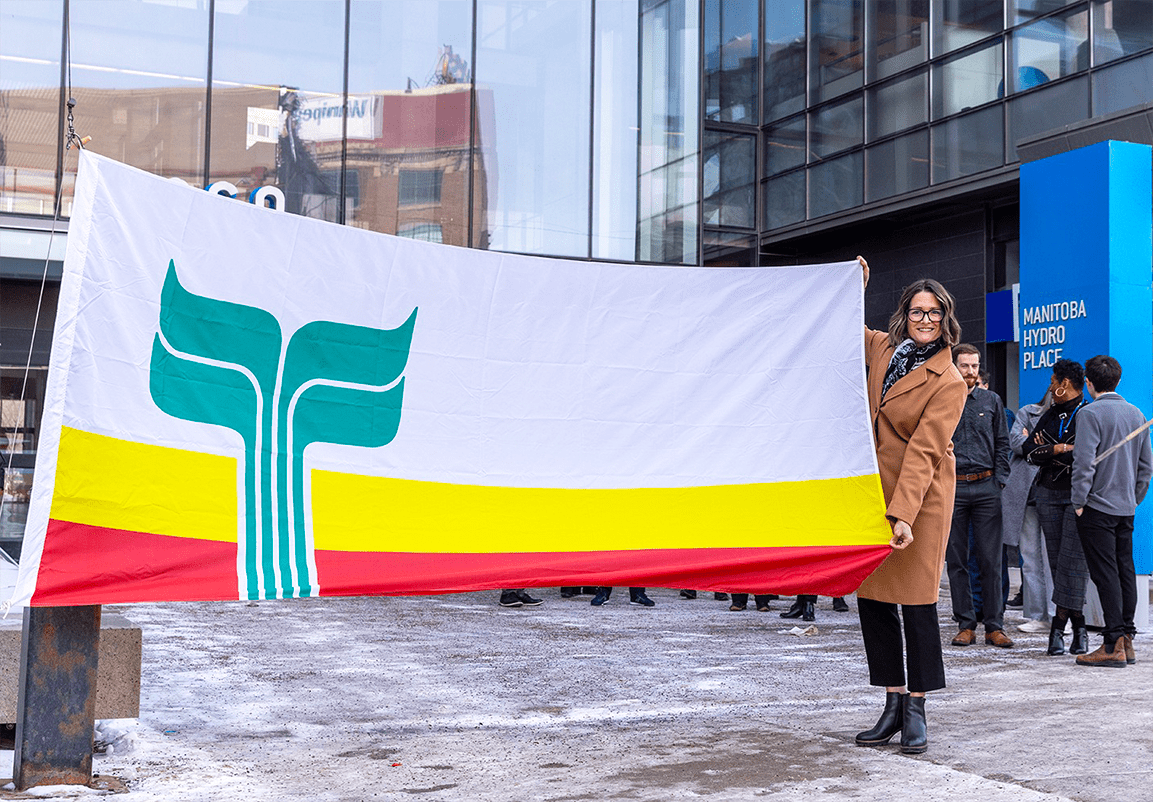 Renée Beaudry, responsable de l’accessibilité et des services en français chez Hydro Manitoba, avec le drapeau franco-manitobain devant les bureaux d'Hydro Manitoba.