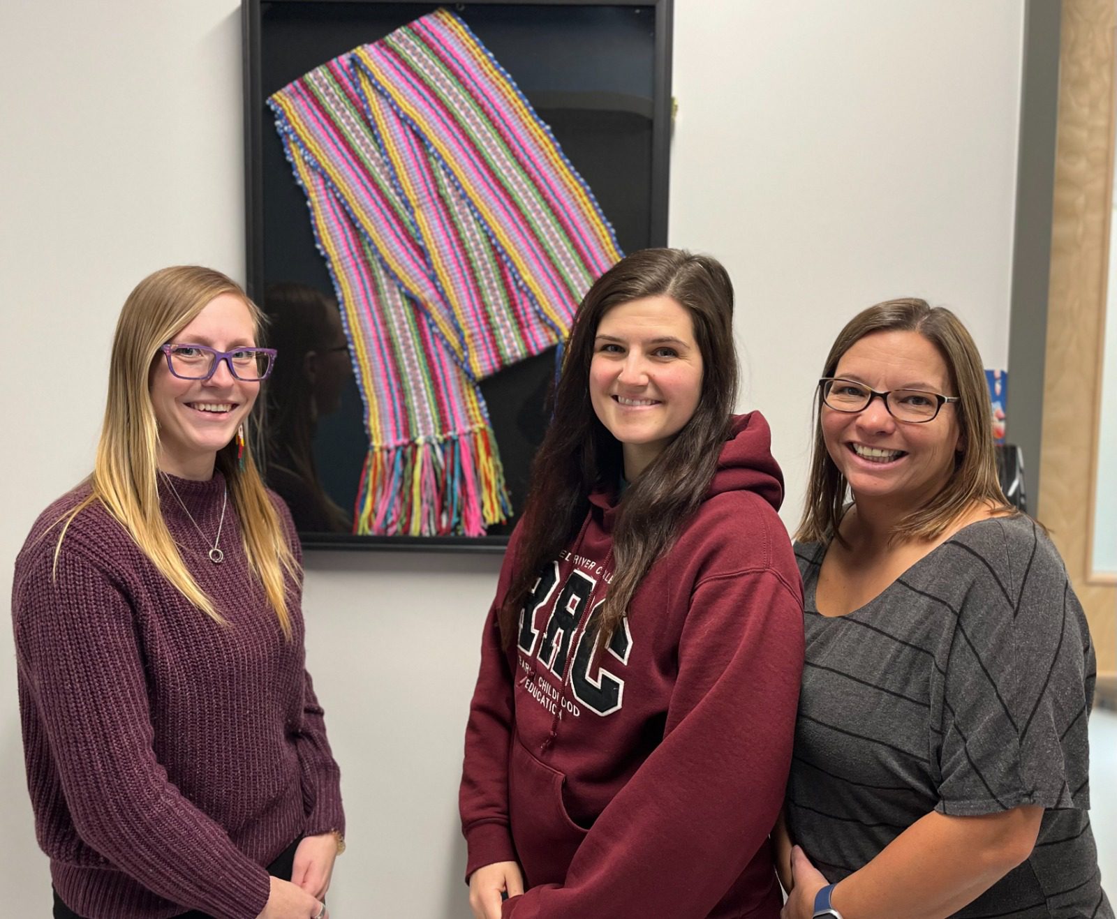 De gauche à droite : Cédelynne Lachance, Jocelyn Fournier, et Rachelle Moroz avec la ceinture fléchée créée par les enfants du centre d'apprentissage francophone Les P’tits Brisous.